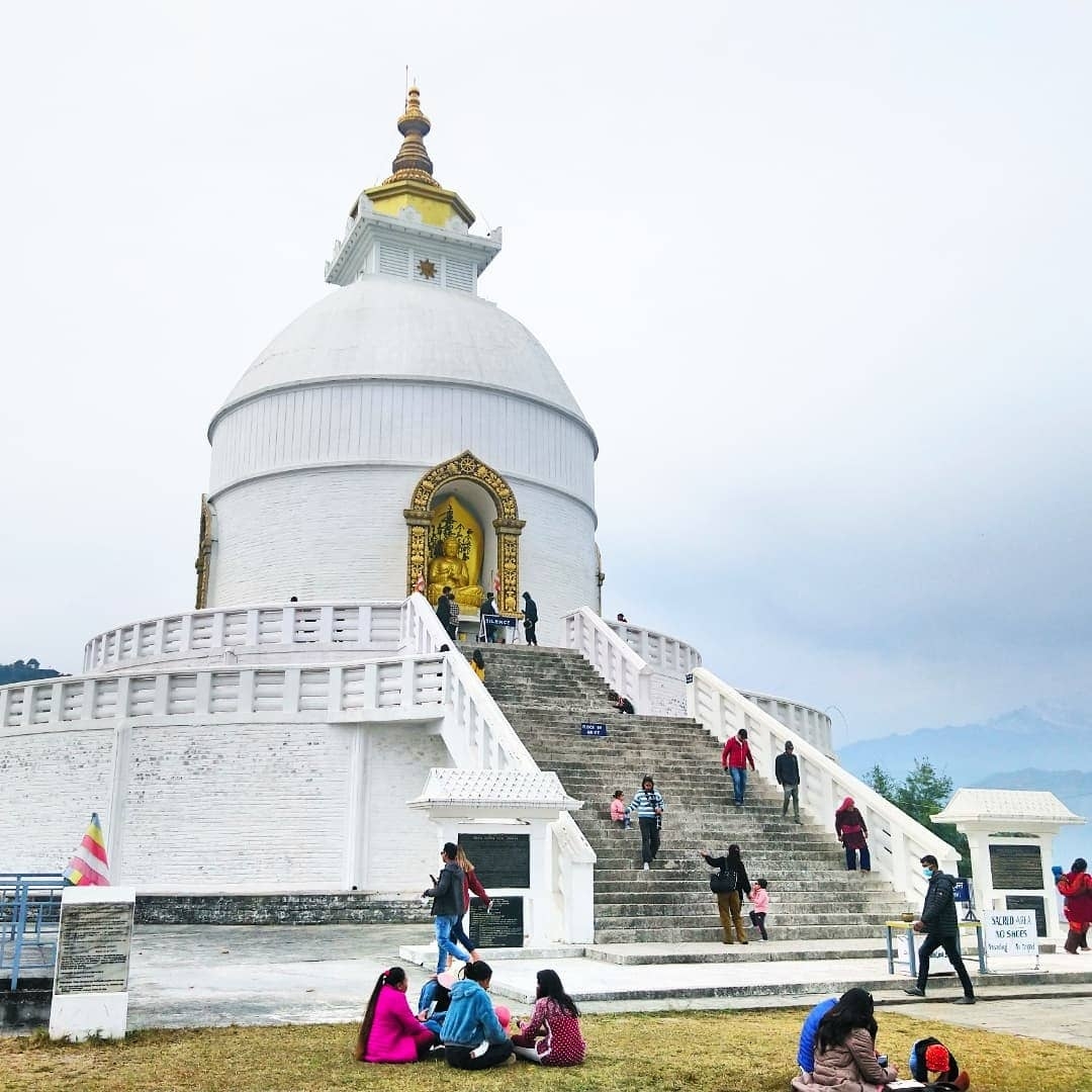 Large white stupa with people at the base and decorative gold elements.