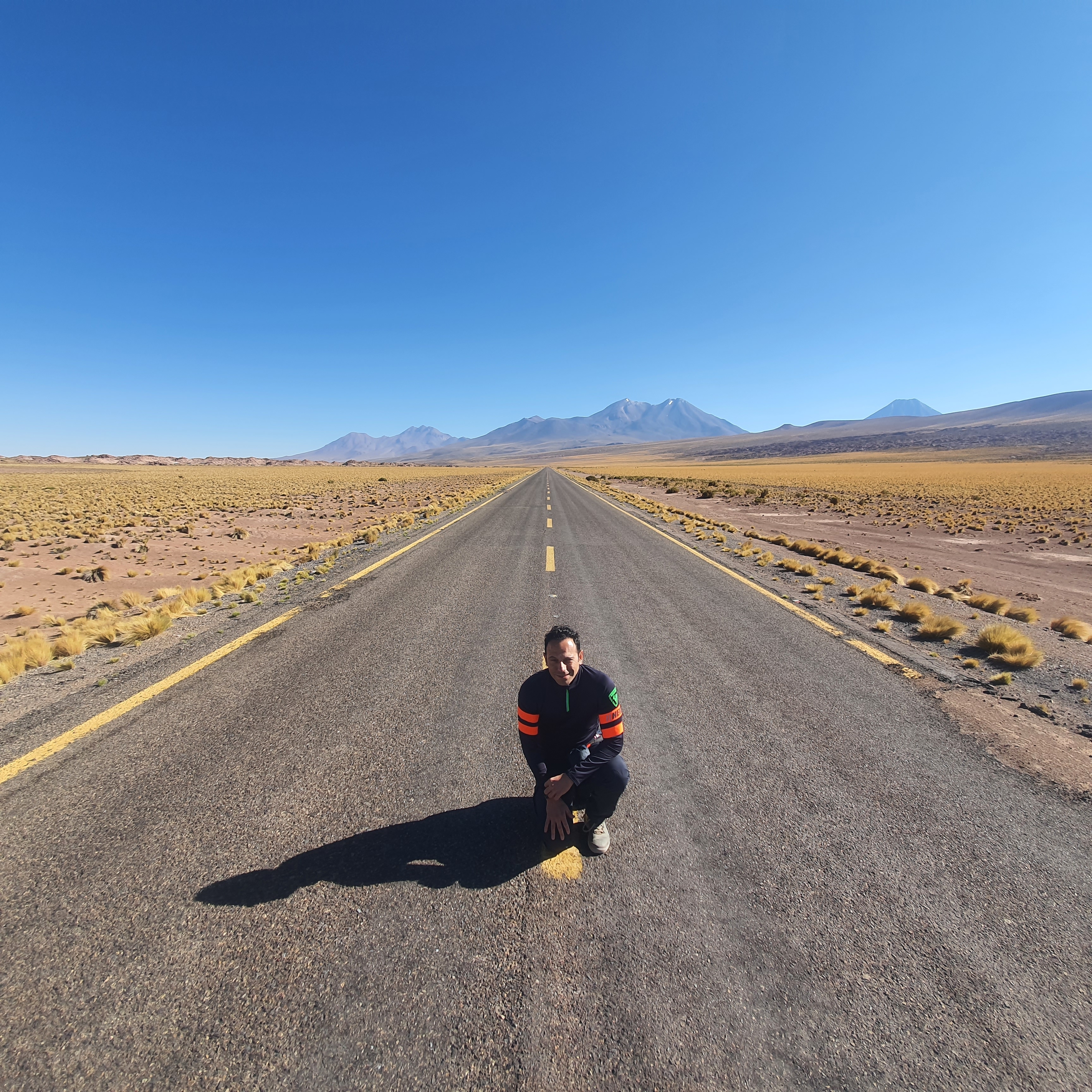 Person kneeling on a long desert road with mountains.