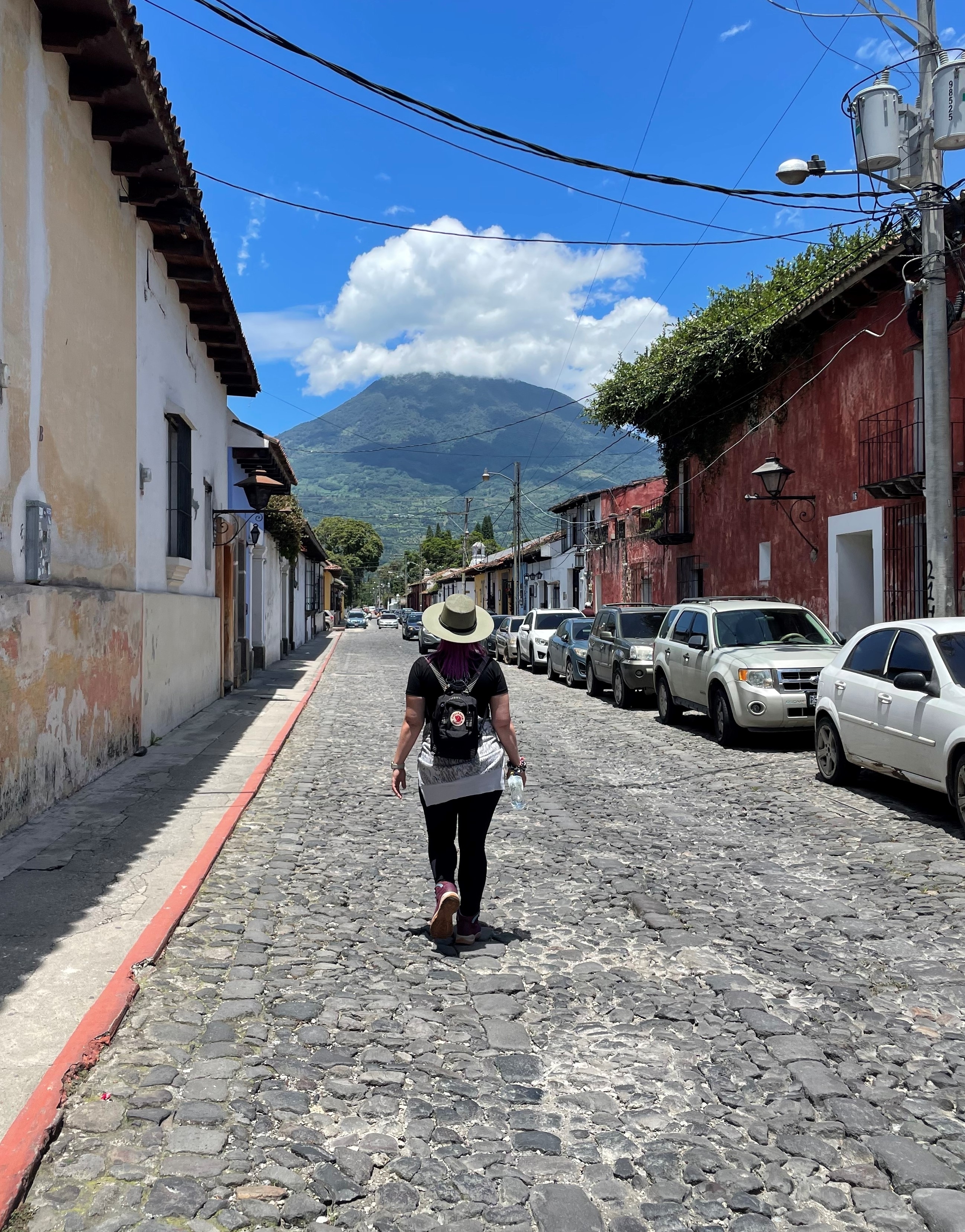 A person walking down a cobbled street with mountains in the background.