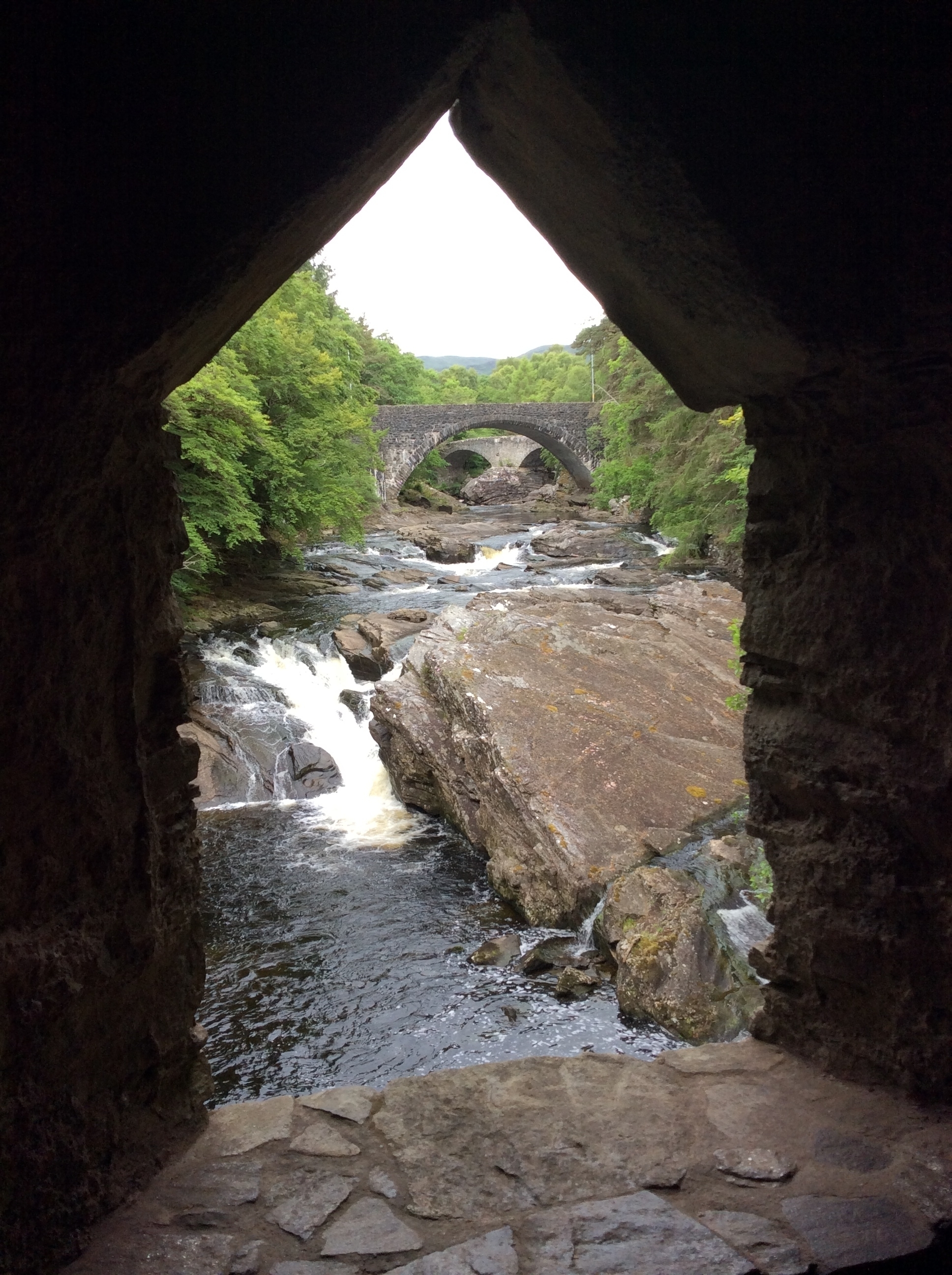 Ancient stone bridge over a river flowing through a forest.