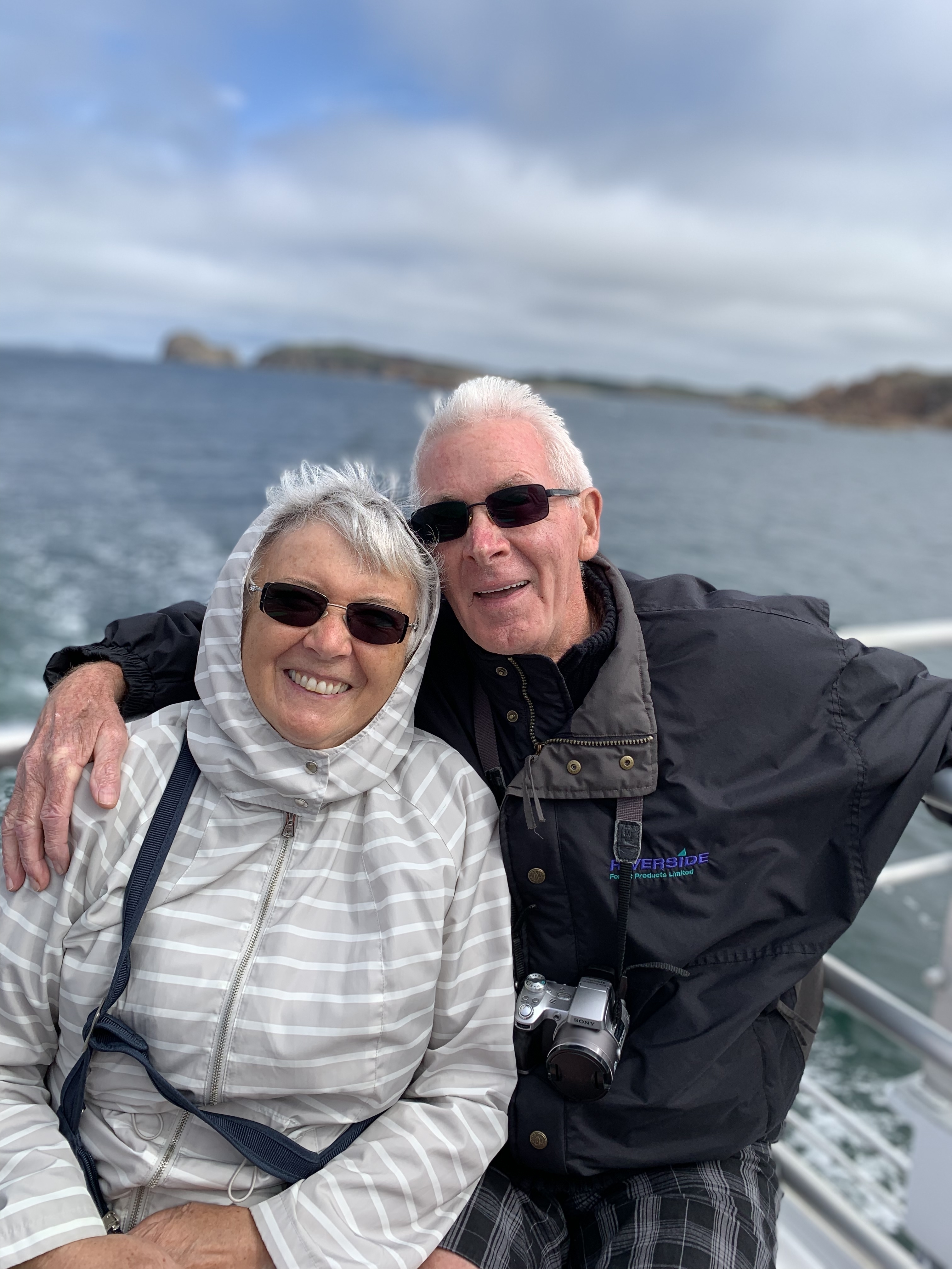Elderly couple smiling on a boat with water in the background.