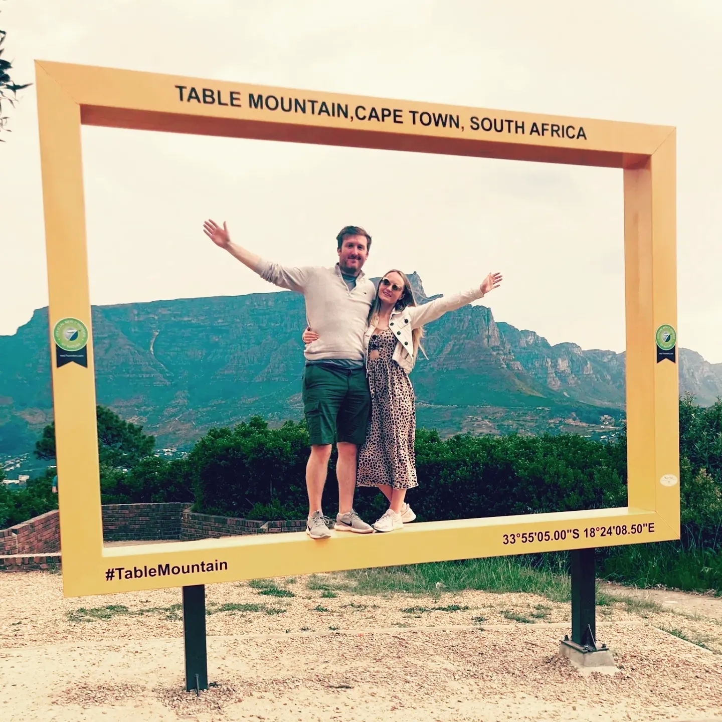 Couple standing in a picture frame with mountain in the background.