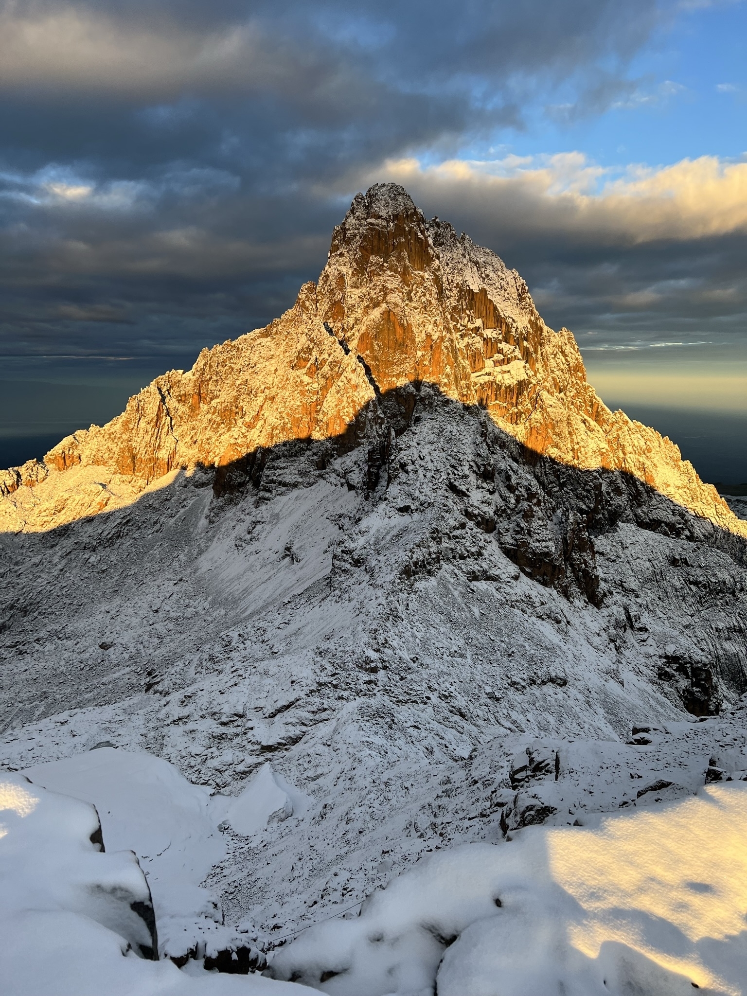 Snow-covered mountain at sunrise with dramatic shadows.