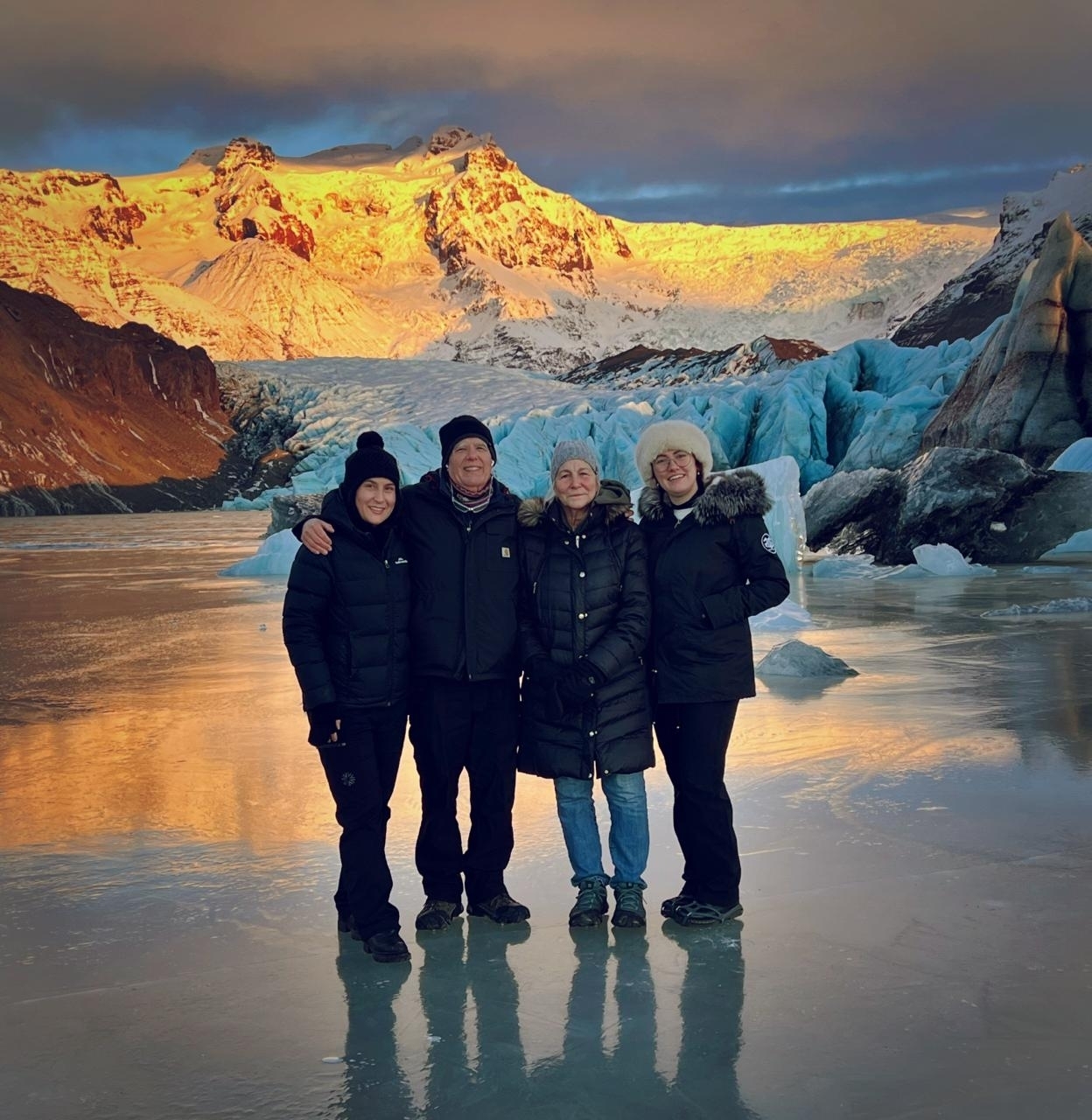 Group photo with people standing on icy ground against glacier background.