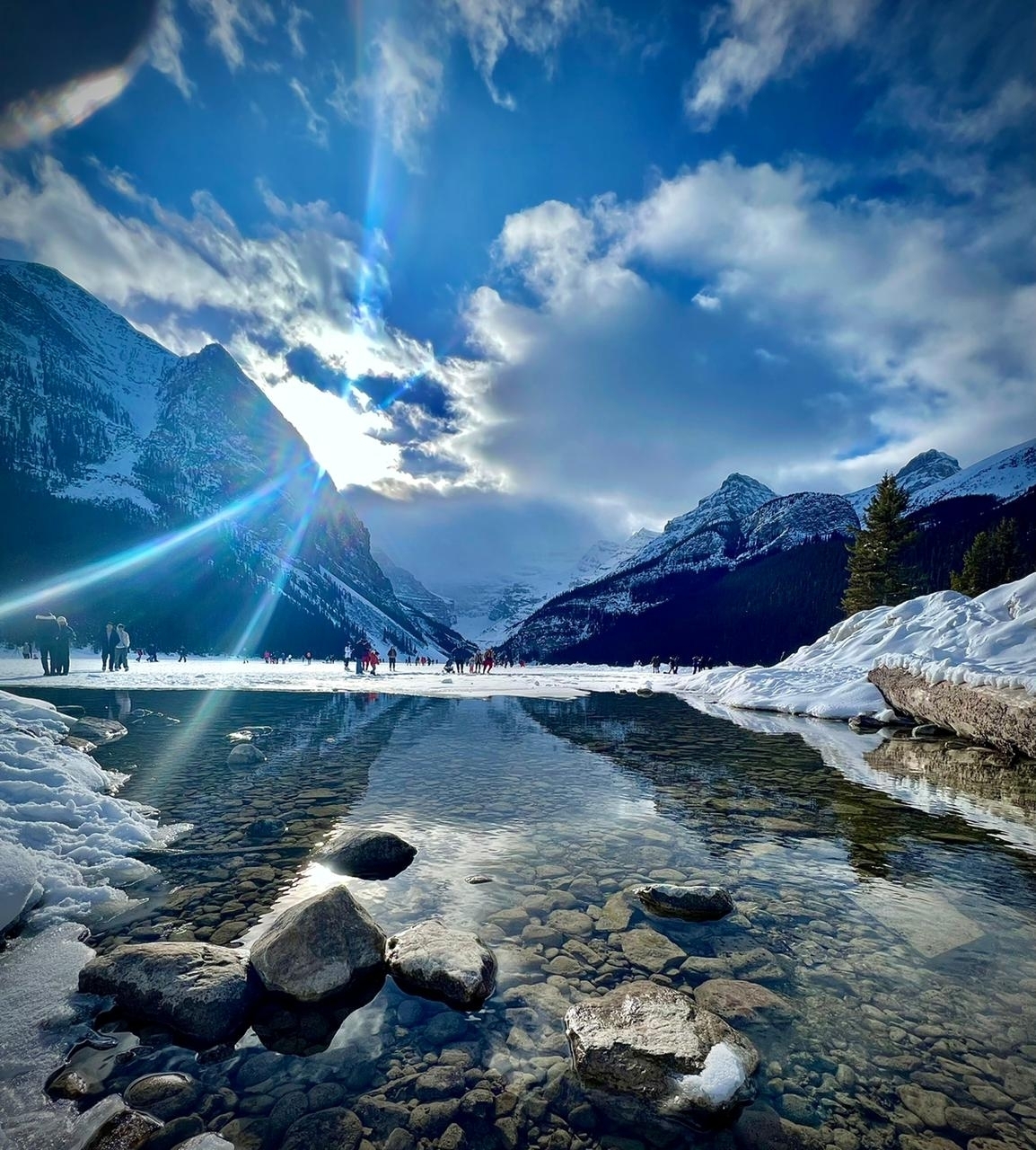 Sun shining over a frozen lake with a dramatic mountain view.