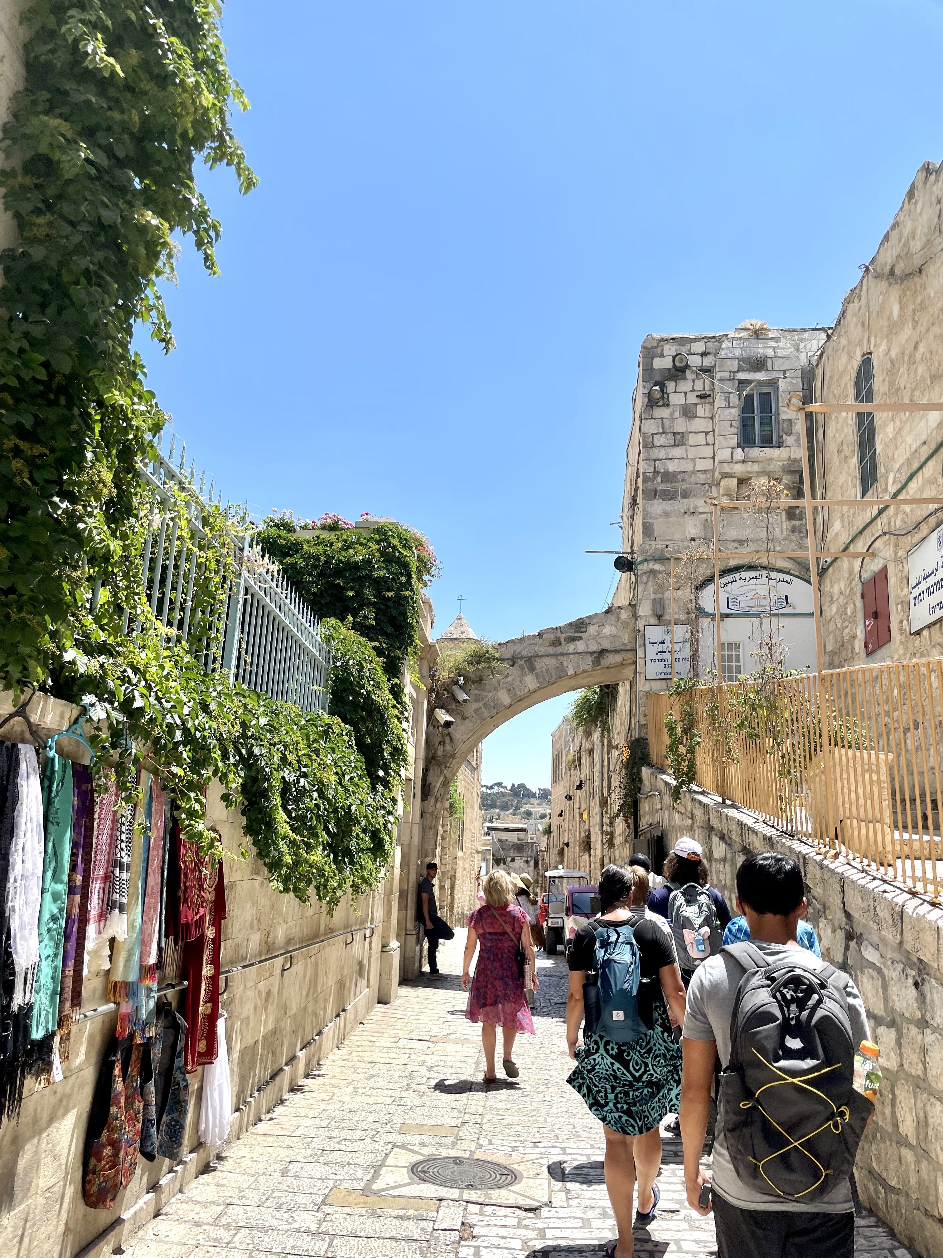 A bustling street with plants and a historic church archway.