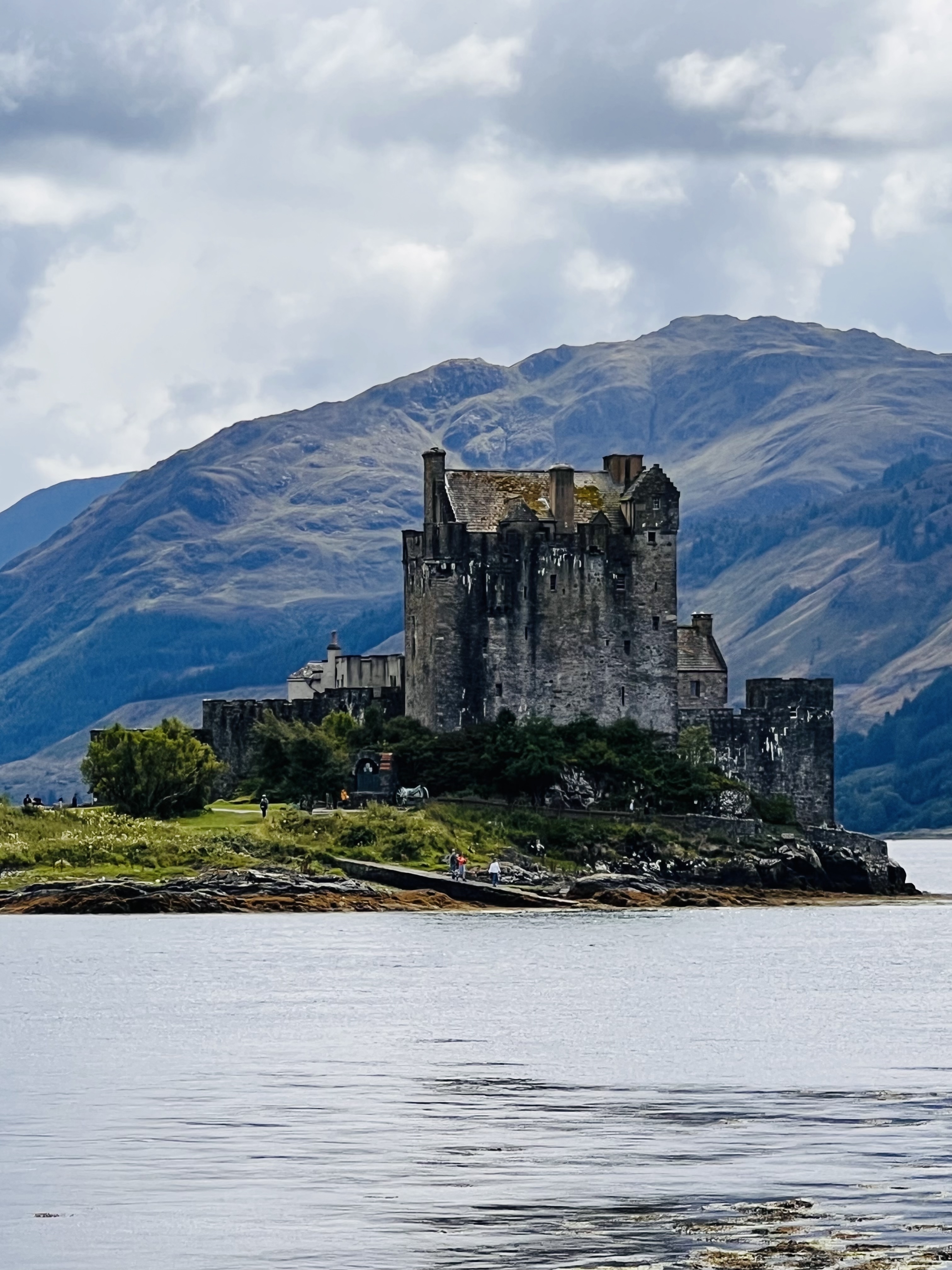 Historic stone castle by the water with mountains in the background.