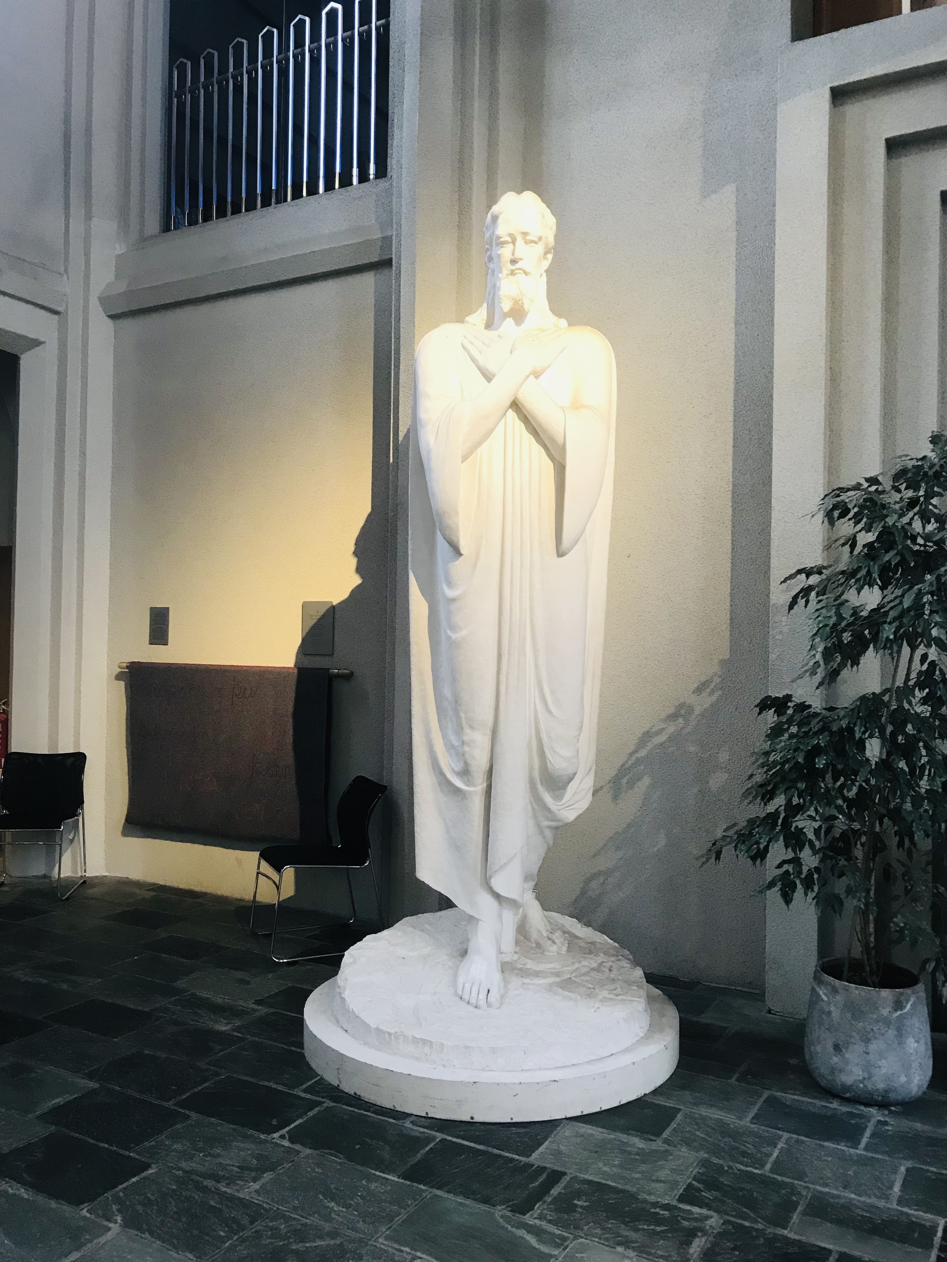 A white statue inside a building, next to a plant.