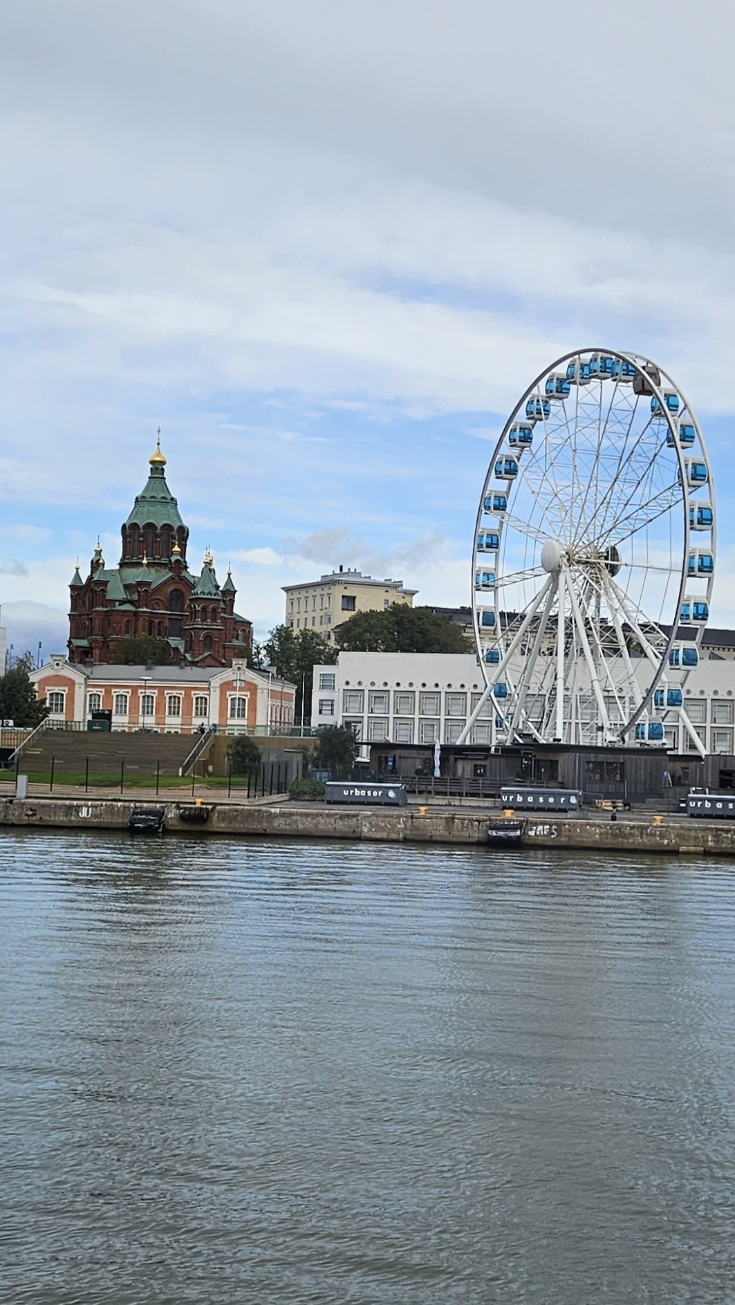 A cityscape featuring a cathedral and a Ferris wheel by a waterfront.