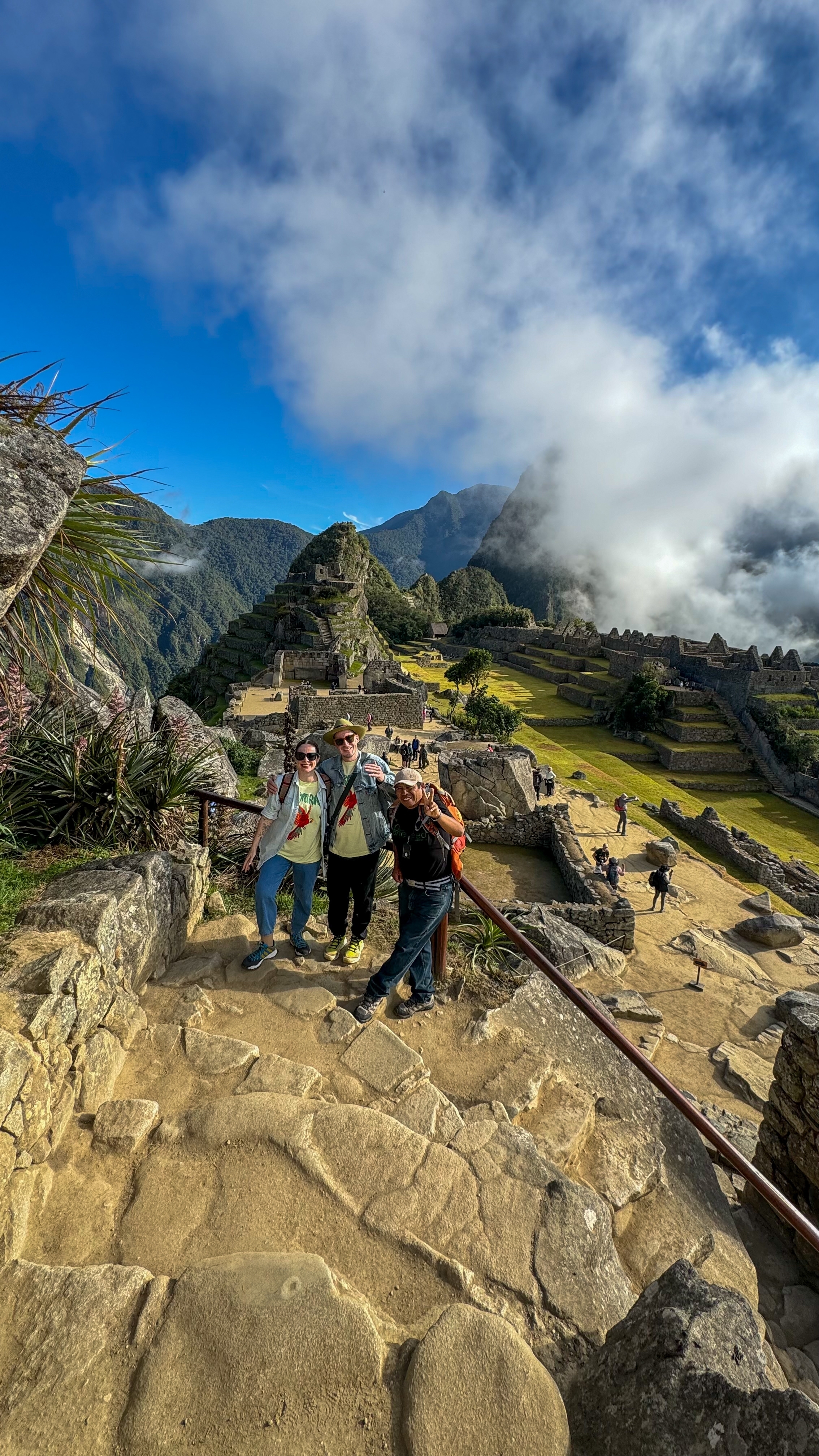 Three people posing at Machu Picchu with ruins and mountains in the background.