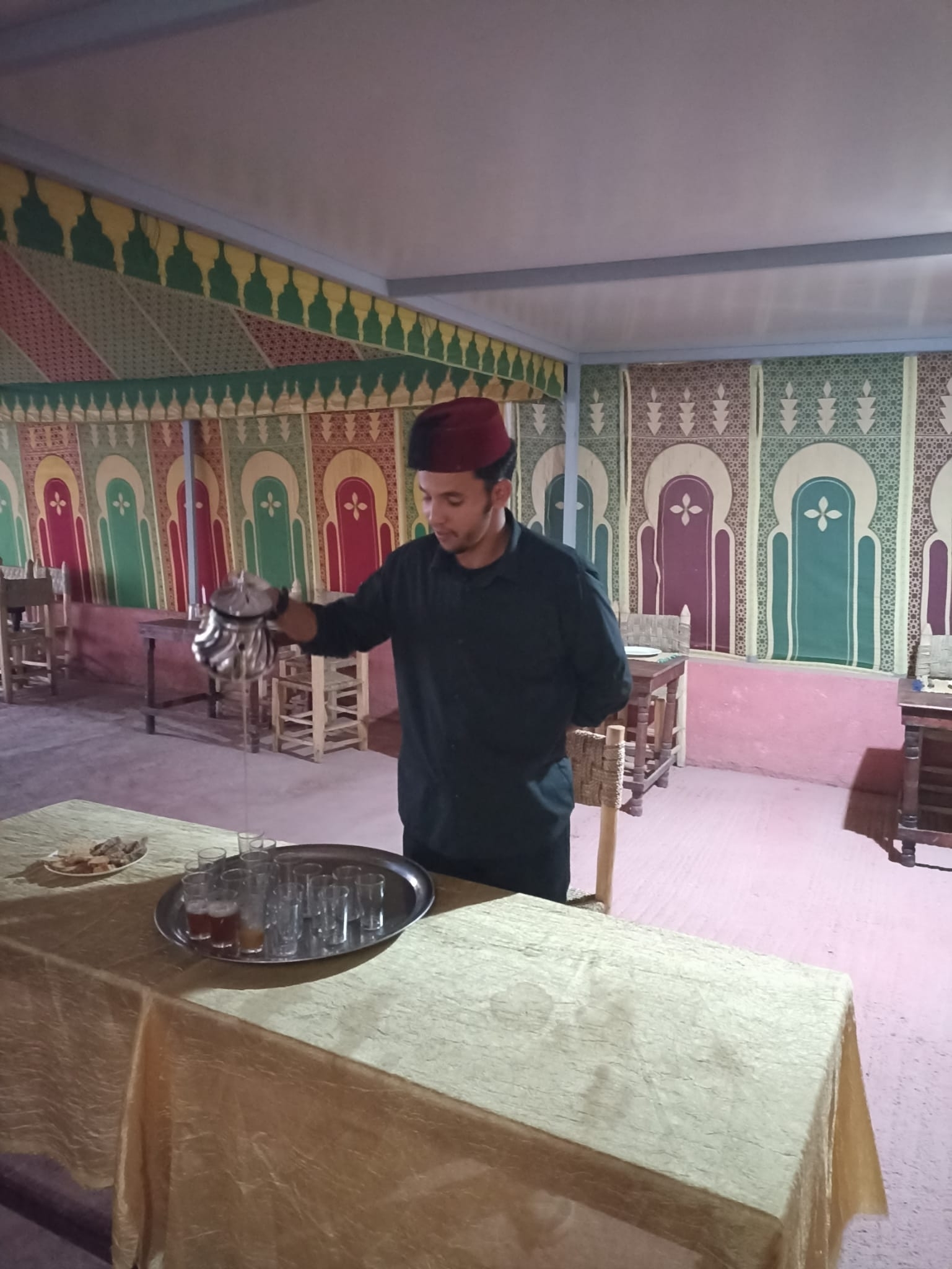 A man in traditional attire pouring tea at a colorful restaurant.