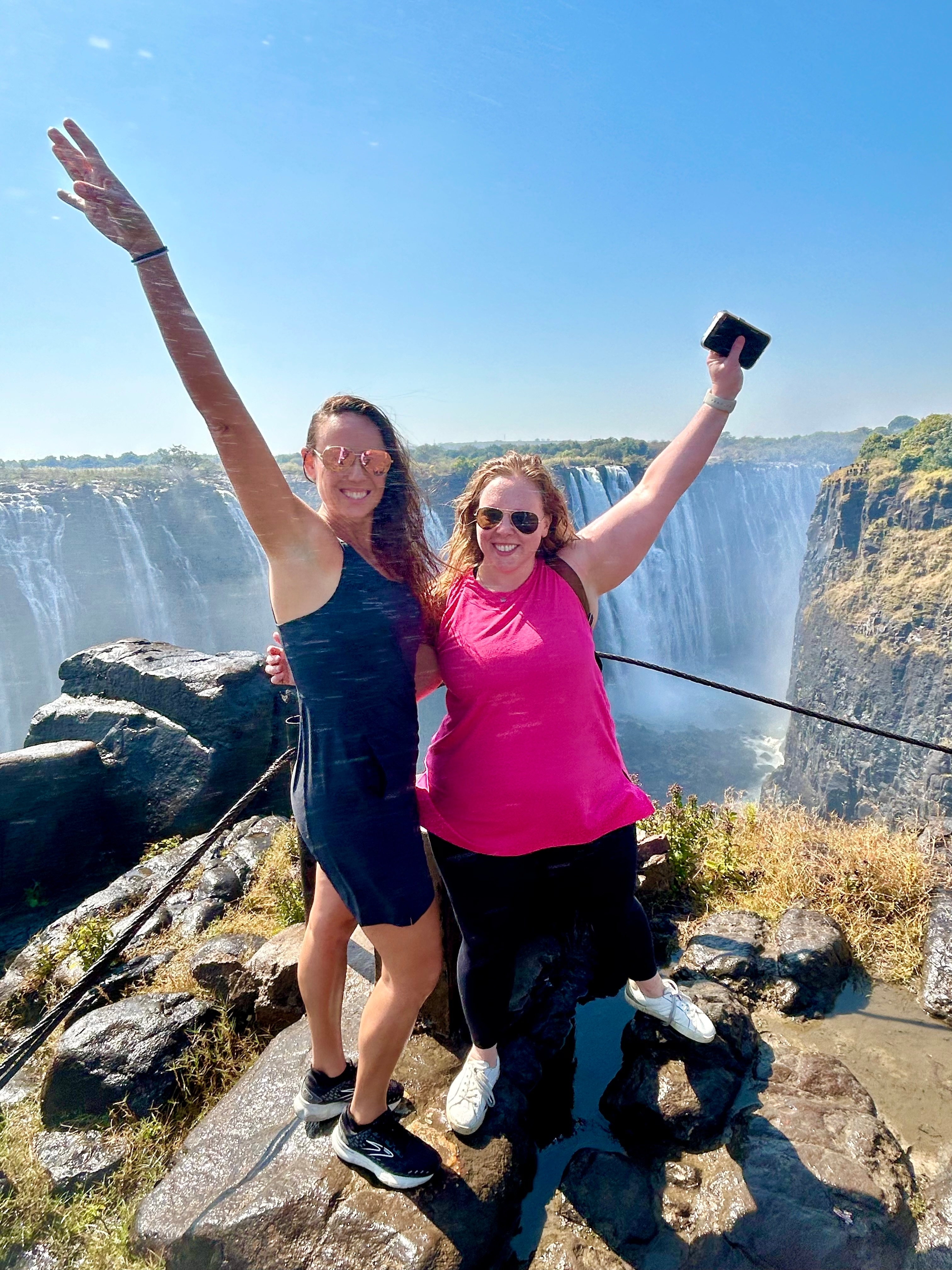 Two women celebrating with Victoria Falls in the background.