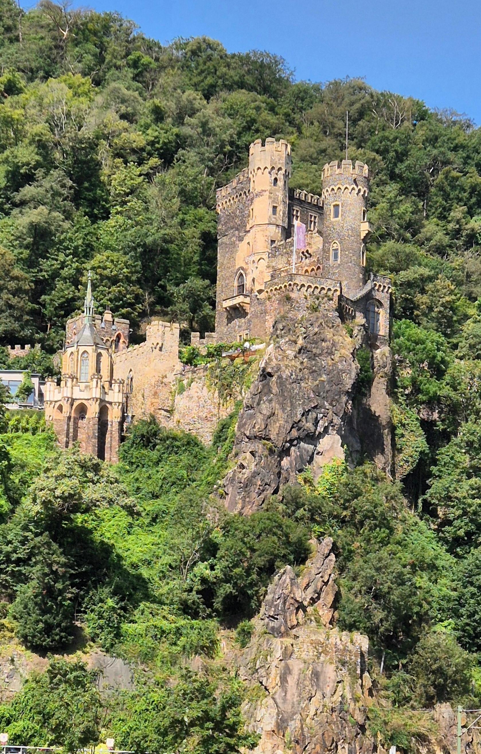 Castle built on rocky terrain surrounded by lush greenery.