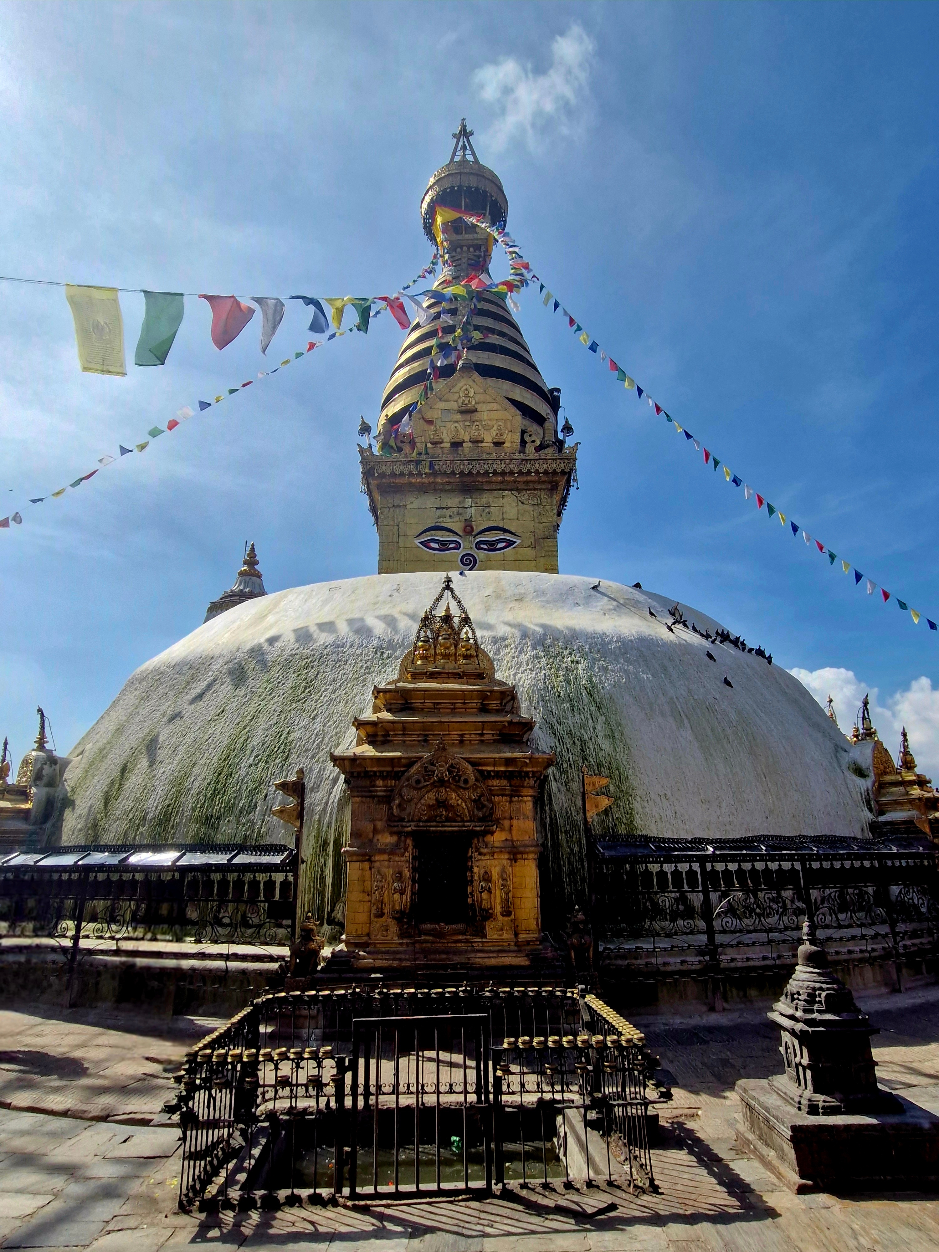 Large stupa with prayer flags against a blue sky.