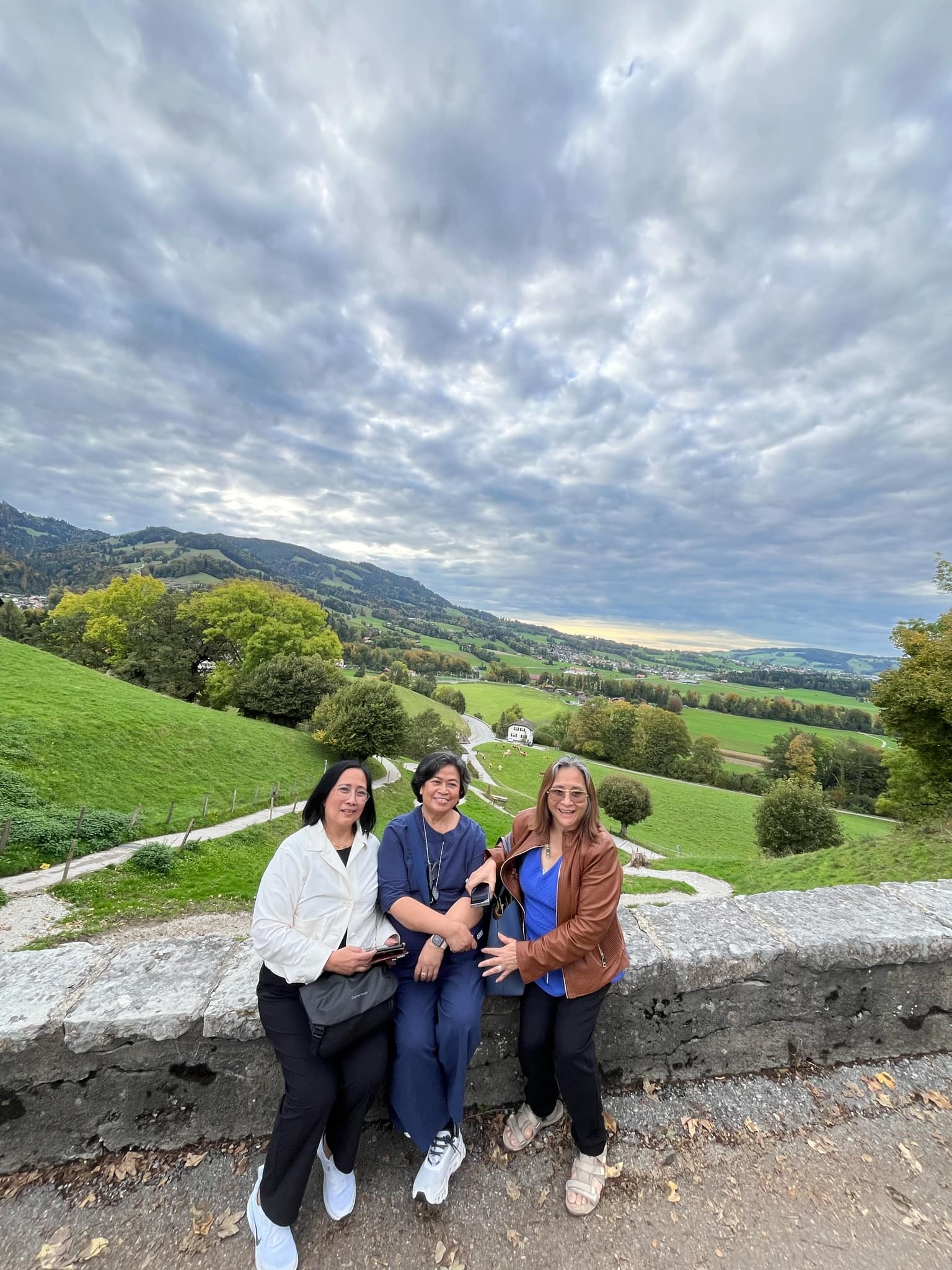 Three people posing in a green landscape with hills and a cloudy sky.