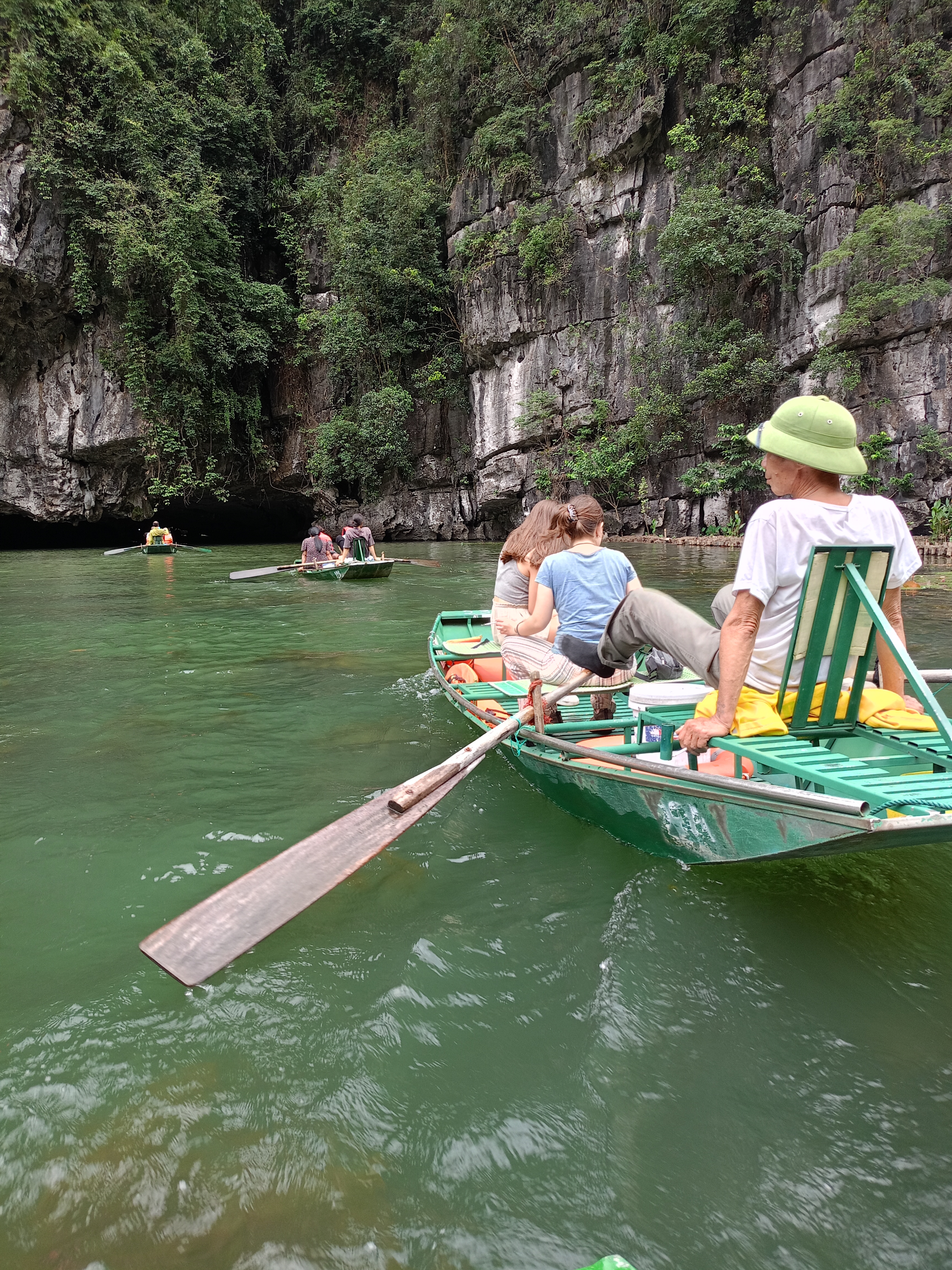 People rowing boats in a clear green river with cliffs