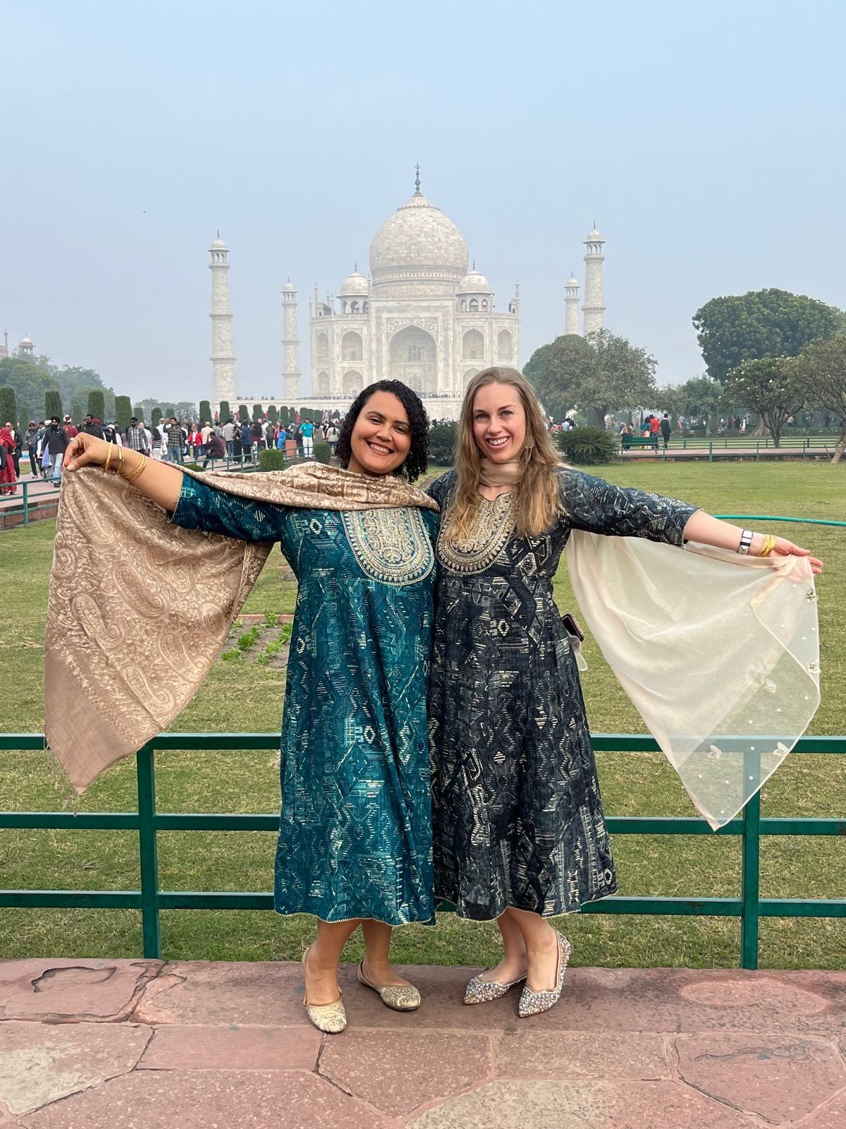 Two women posing in front of the Taj Mahal wearing traditional attire.