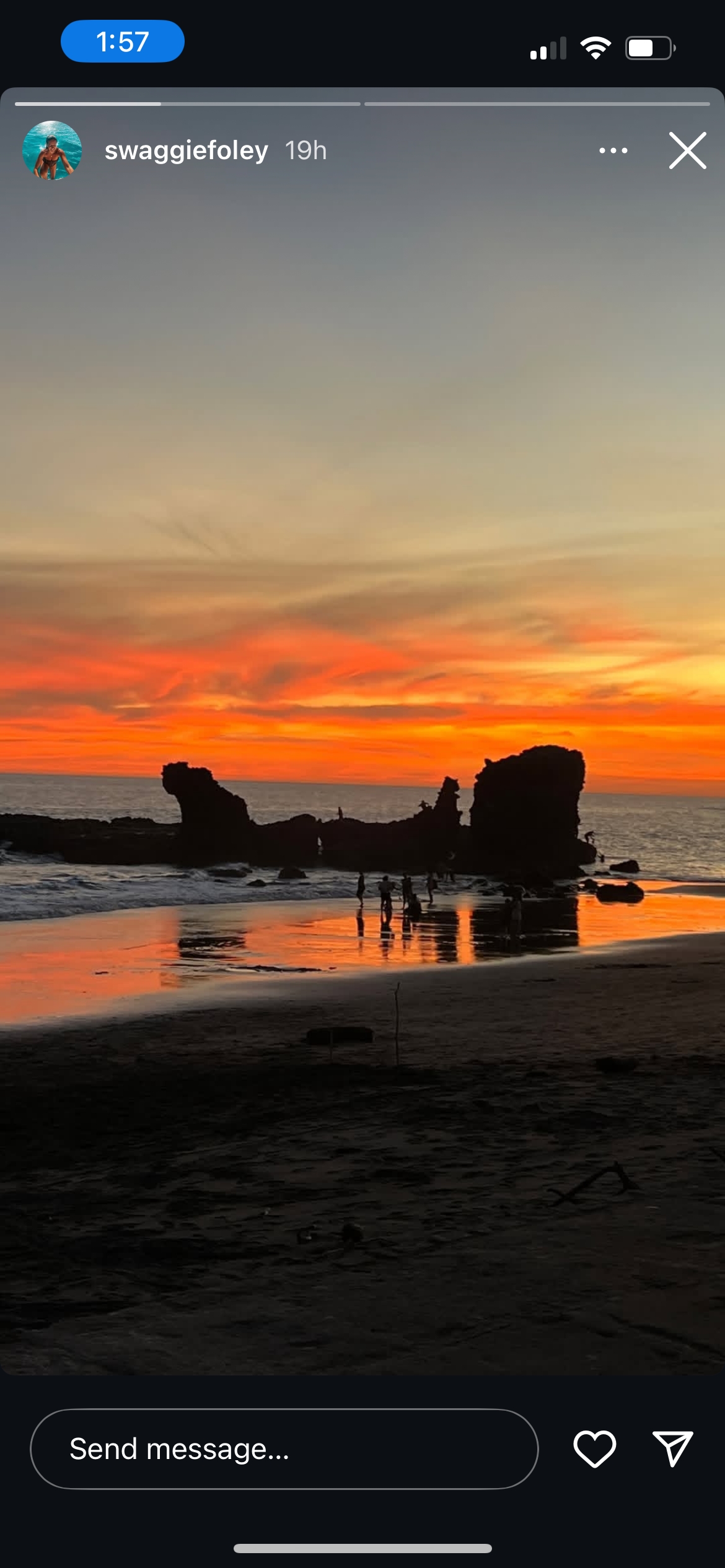 A beach during sunset with silhouettes of people and rocks.