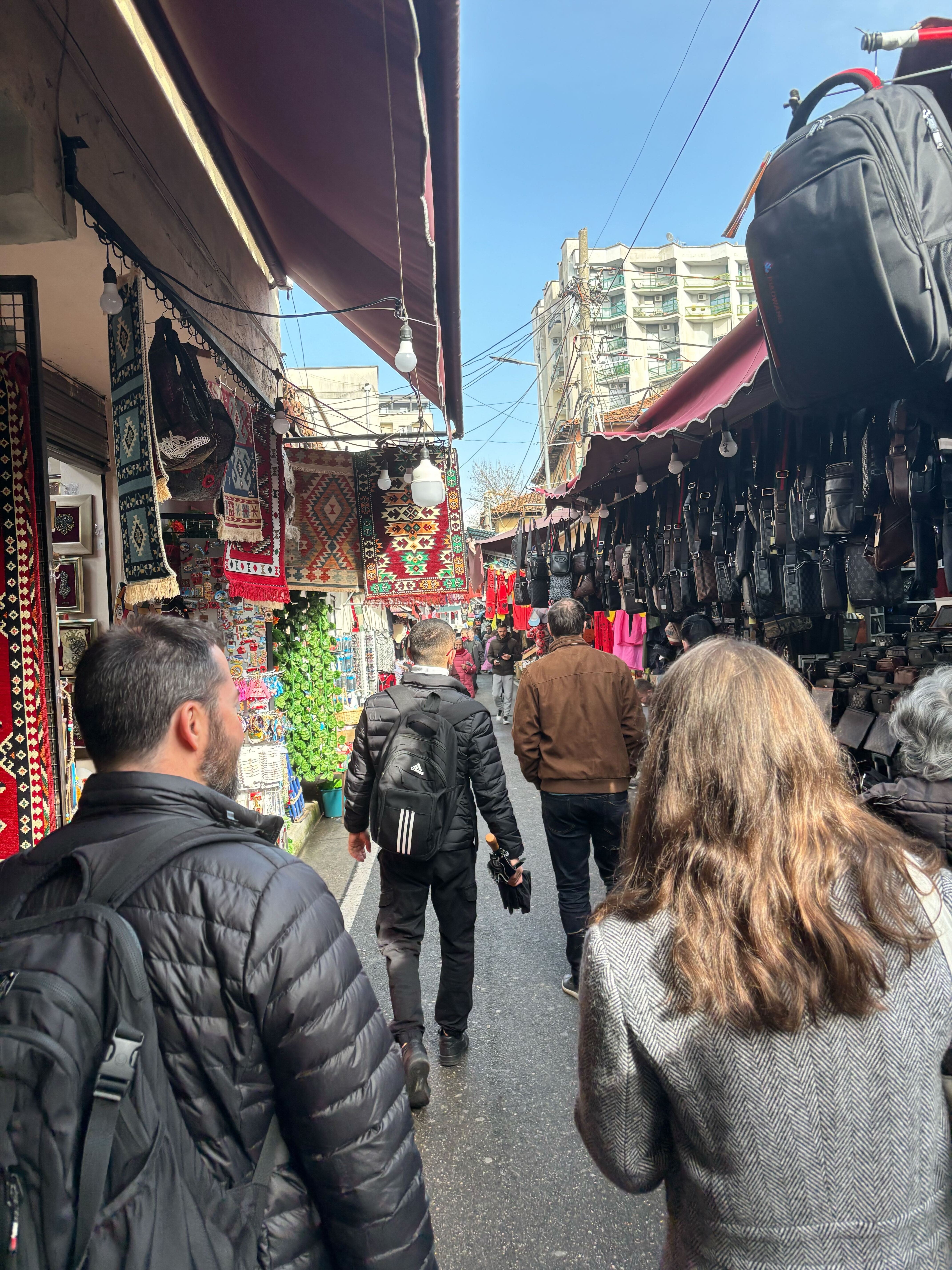 Market alley with people and colorful textiles hanging.