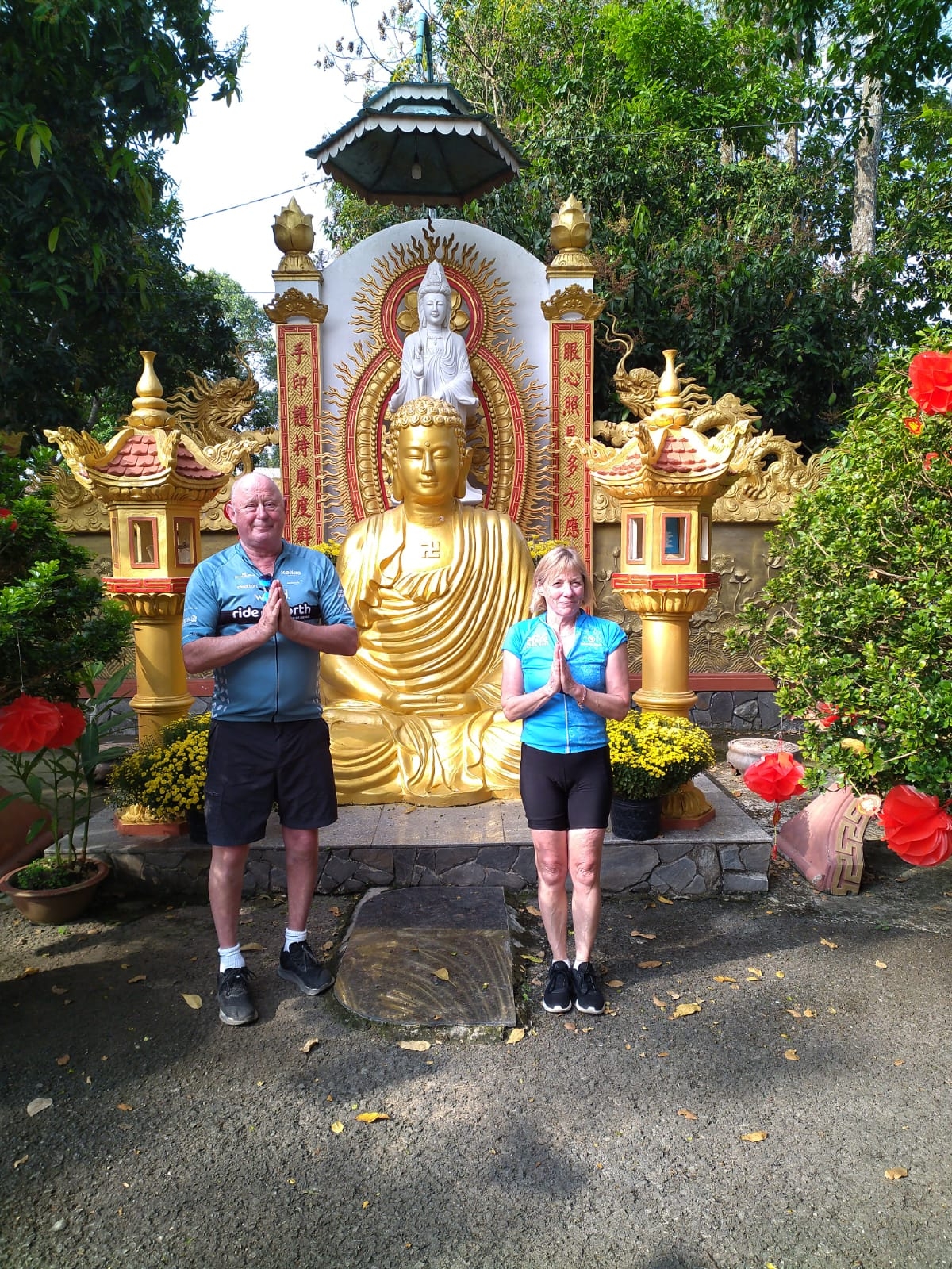 Two people posing in front of a golden Buddha statue.