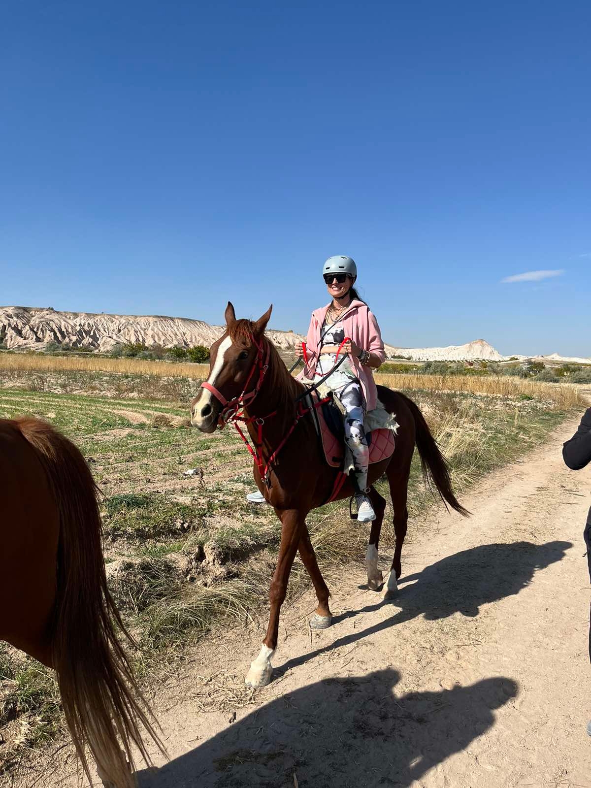 Person riding a horse on a dirt path with rocky hills in the background.