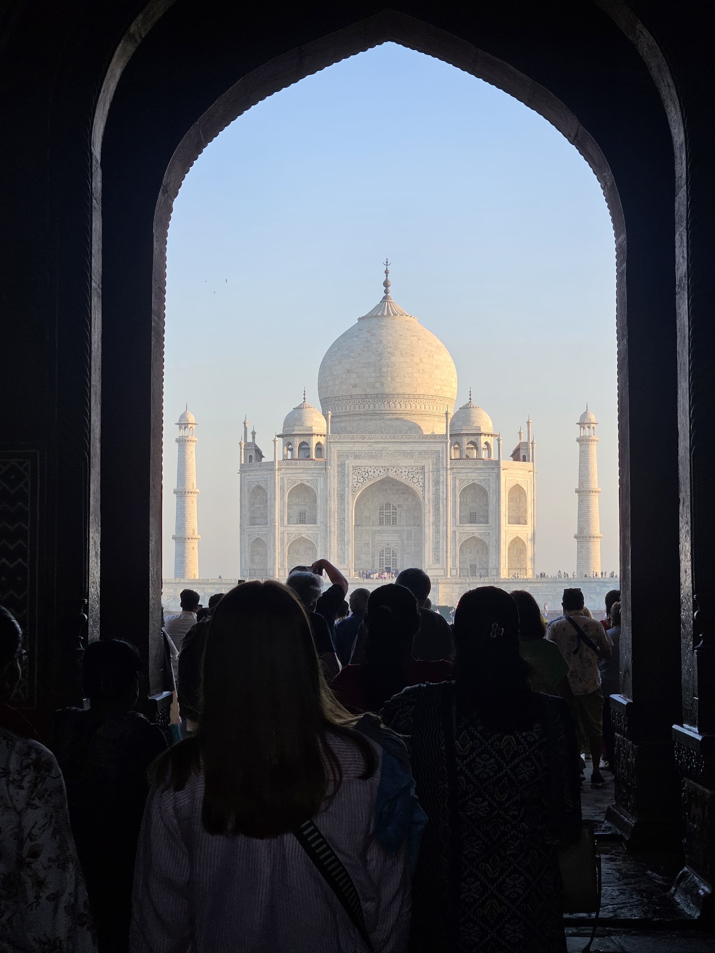 Taj Mahal viewed through an archway, crowded with tourists.