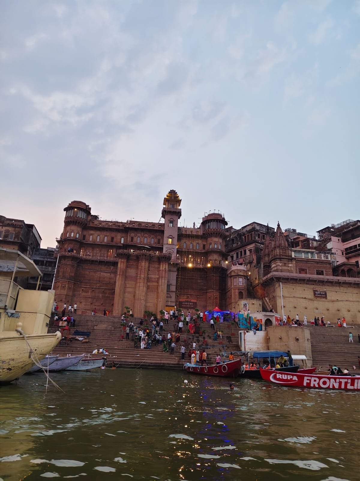 Populated ghat area near a historic structure at dusk.