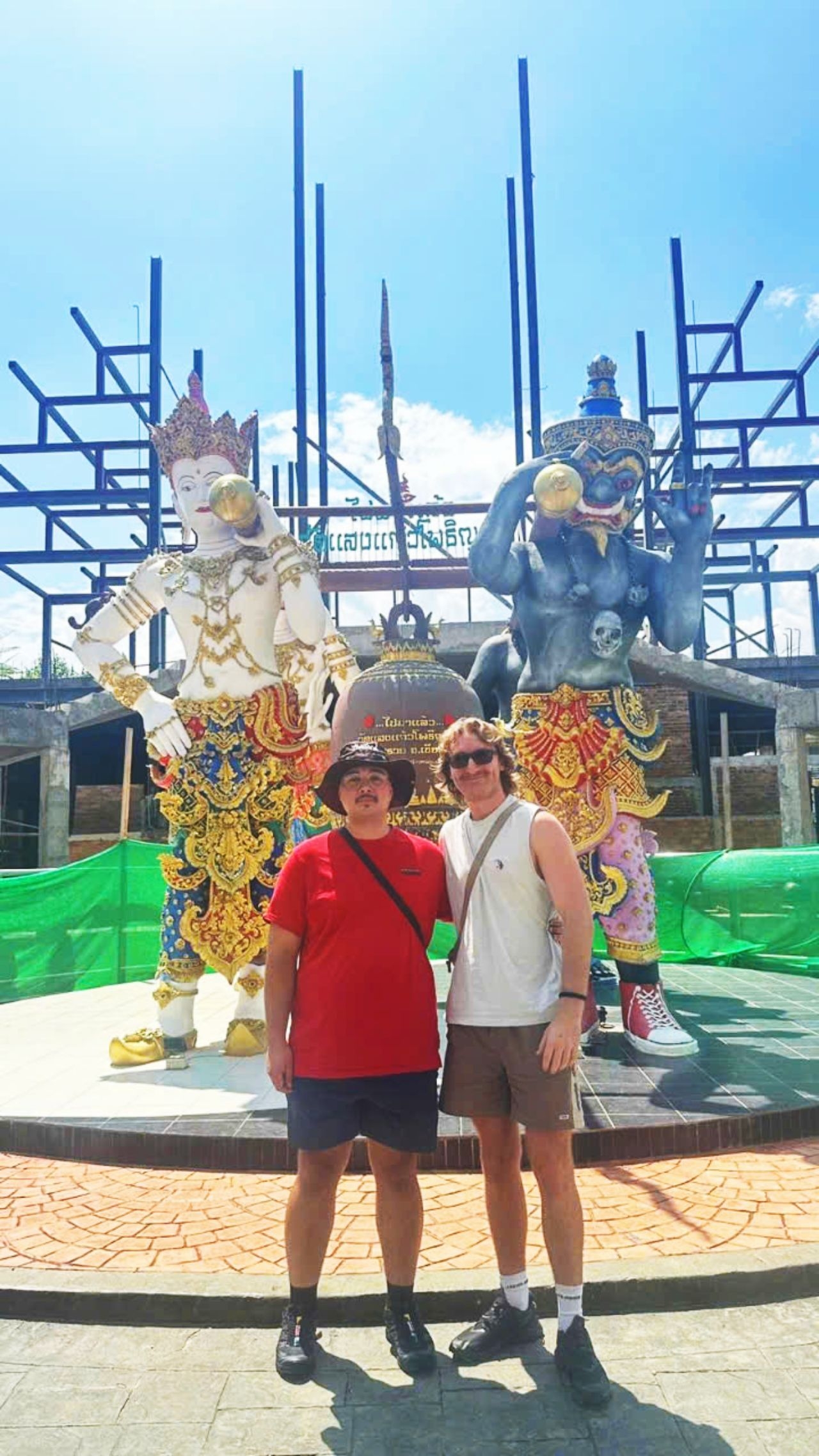 Two men posing in front of colorful statues at a temple.
