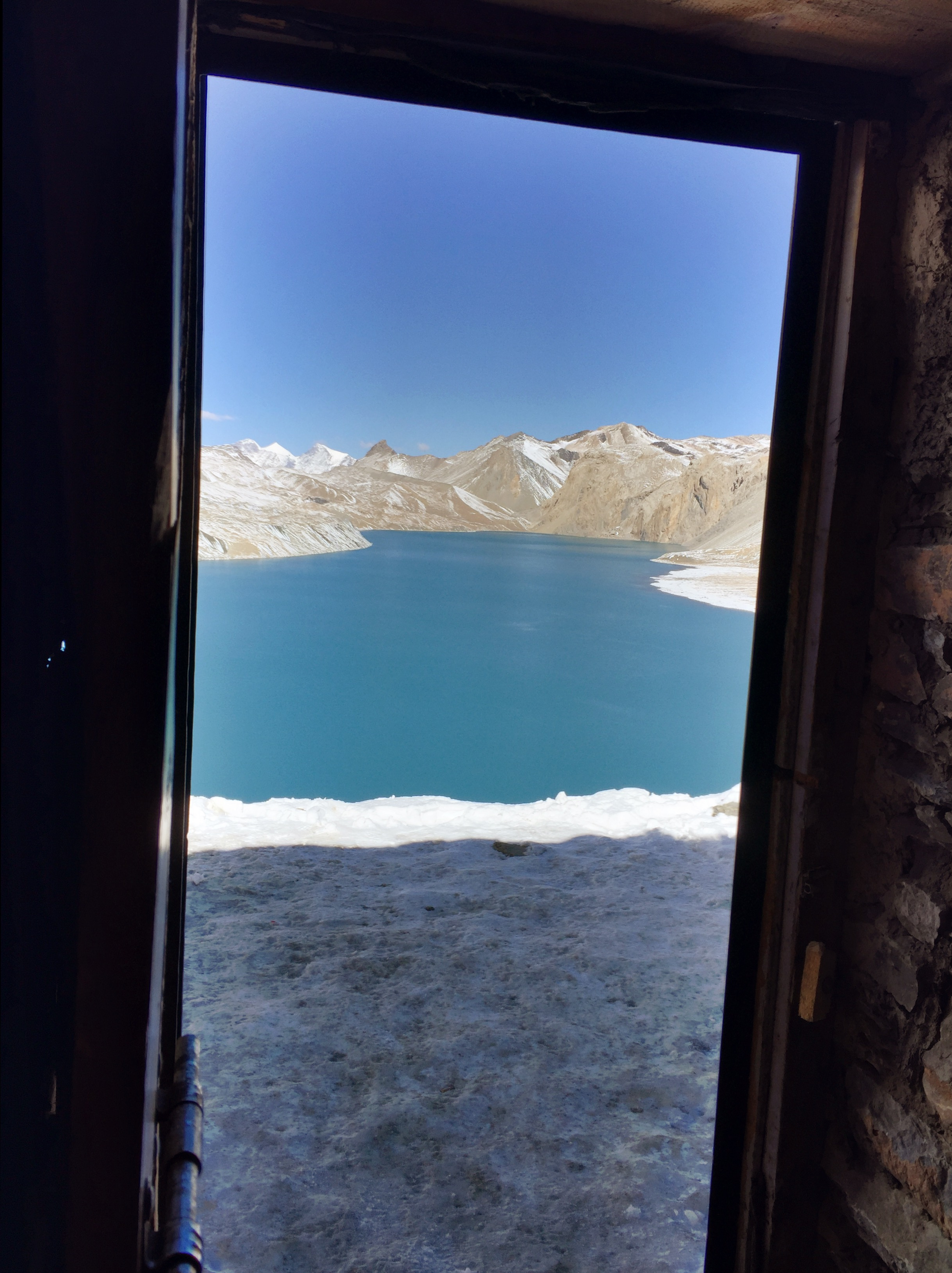 Scenic view of a blue lake surrounded by mountains, viewed from a doorway.