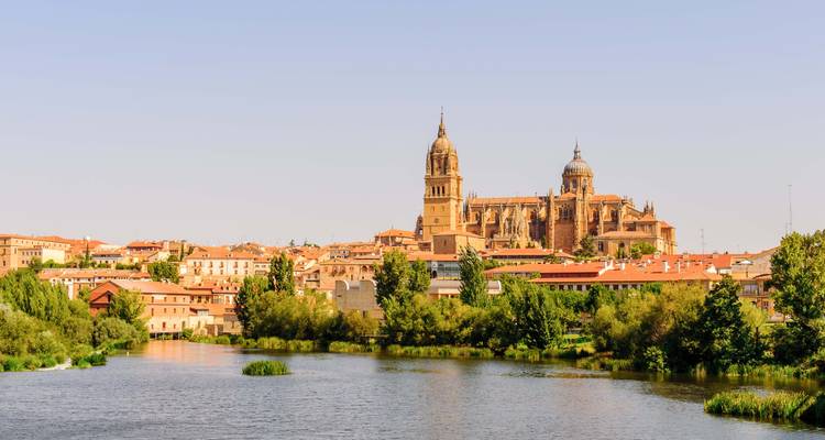 Paysage urbain mettant en vedette une grande cathédrale et une rivière tranquille, sous un ciel dégagé.