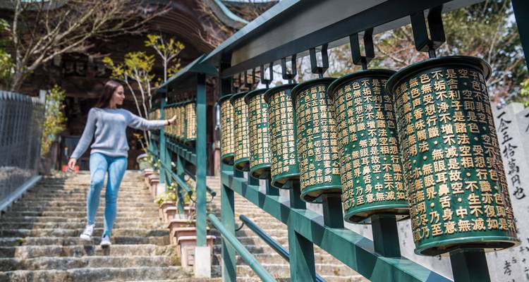 Un viajero pasa frente a una fila de cilindros giratorios de oración inscritos con caracteres kanji dorados en las escaleras del templo.
