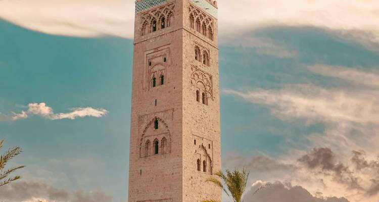 Hoge minaret tegen een blauwe lucht met wolken.