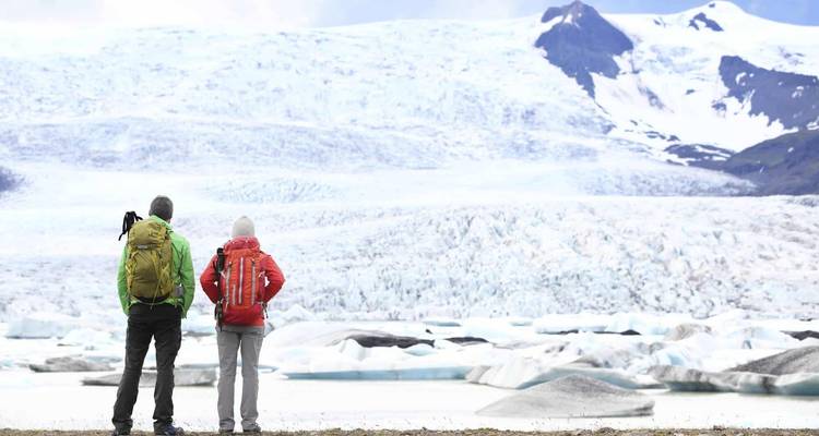 Dos personas paradas frente a un vasto glaciar.