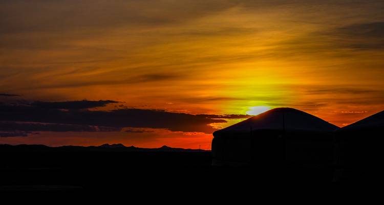 Gers mongoles recortados contra un atardecer naranja vibrante sobre la estepa.