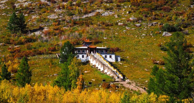 Pequeño monasterio en la ladera anidado entre árboles de otoño con una larga escalera blanca que sube.