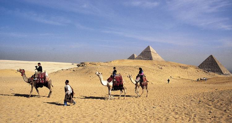 People riding camels near the pyramids in the desert.
