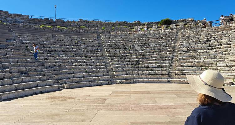 Visitor explores the stone tiers of an ancient Greek amphitheater under blue sky.