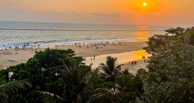 Strand bei Sonnenuntergang mit Menschen und Palmen.