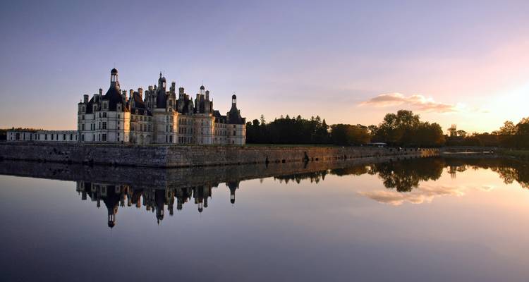 Schloss bei Sonnenuntergang mit Spiegelung im Wasser.