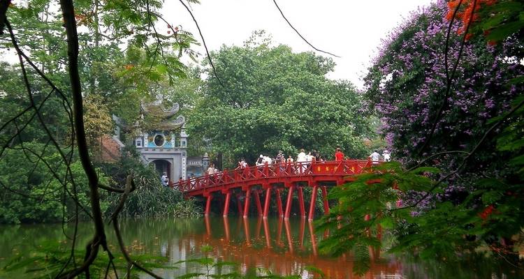Puente de madera roja sobre un lago verde con un entorno exuberante.