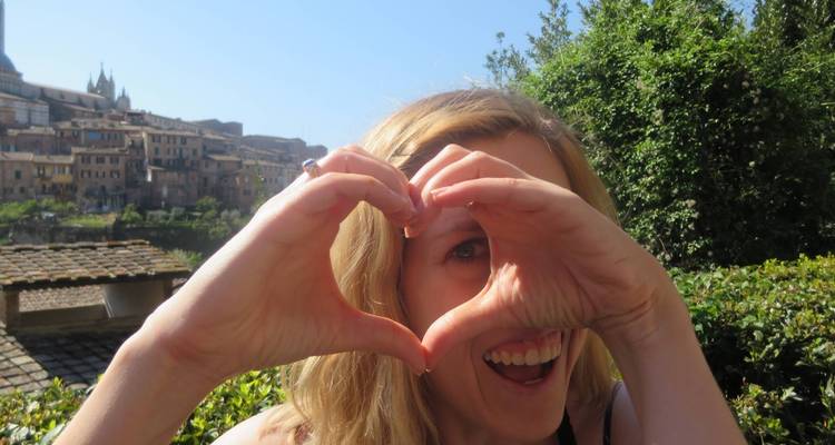 Mujer haciendo forma de corazón con las manos y sonriendo con una ciudad detrás.