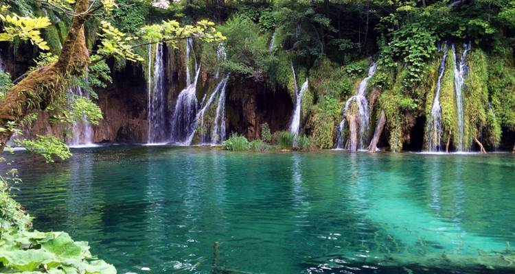 Watervallen die neerstorten in een heldere turquoise meer omringd door weelderige groen.