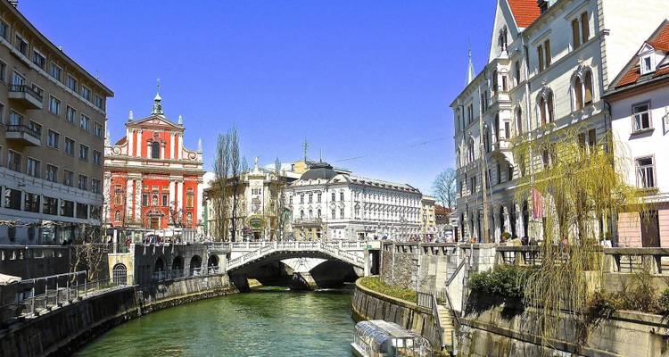 Kleurrijke stadsgebouwen langs een rivier met een stenen brug in Ljubljana.