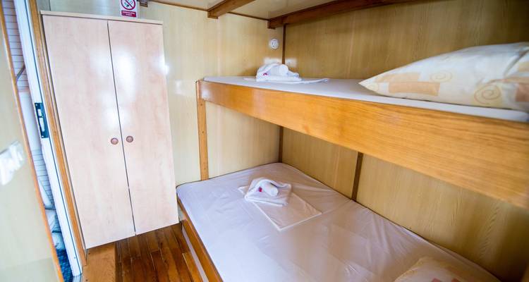 Intérieur de cabine de bateau avec lits superposés et une armoire.