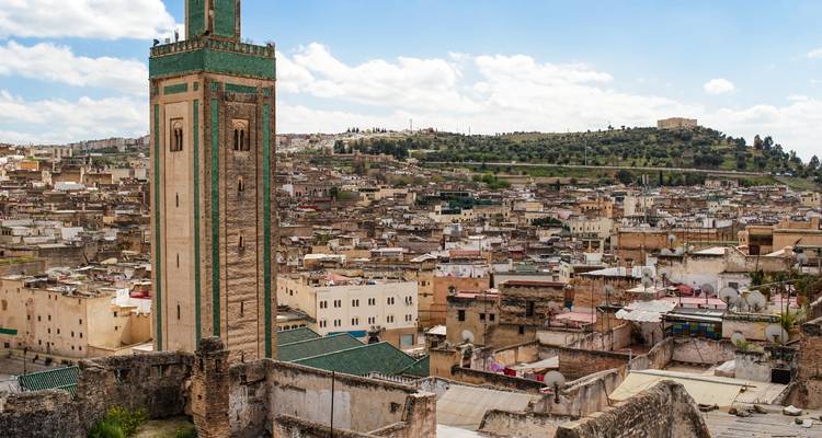 Panoramic view over the densely packed medina of Fes with tall green-tiled minaret in foreground