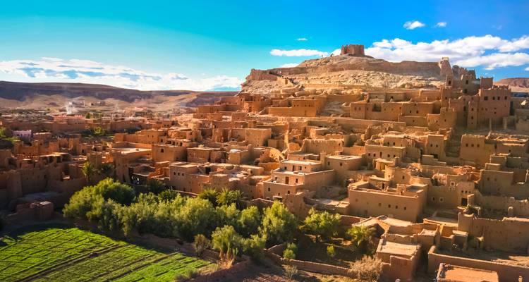 Ancient earthen kasbahs of Ait Benhaddou clustered on a hilltop with lush green fields below