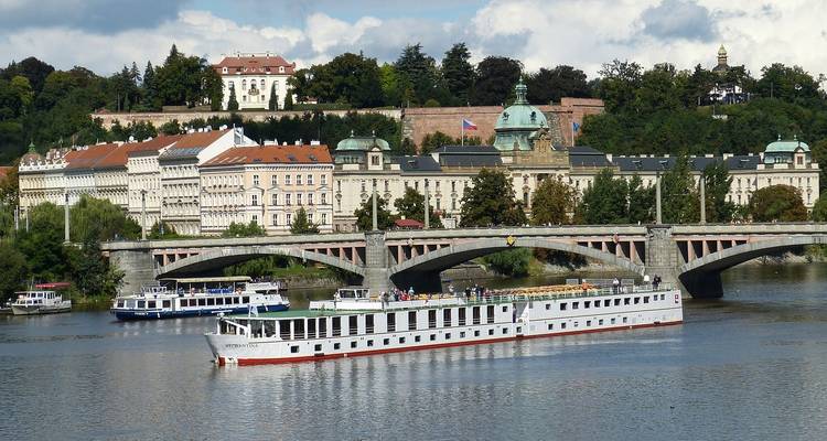 Crucero deslizándose por el río Moldava pasando por edificios históricos ornamentados y puentes en Praga.