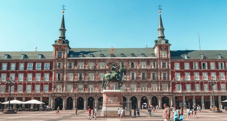 Plaza Mayor in Madrid with equestrian statue, arcaded red buildings and tourists.
