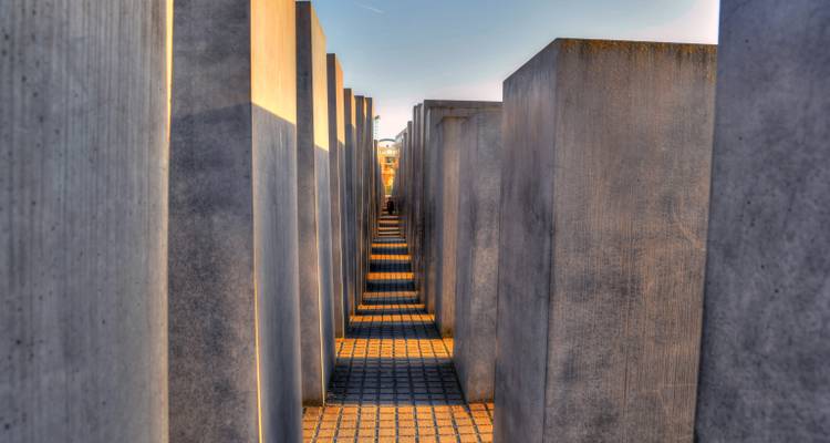 Pasillo simétrico entre estelas de concreto en el Memorial del Holocausto de Berlín bajo luz cálida.
