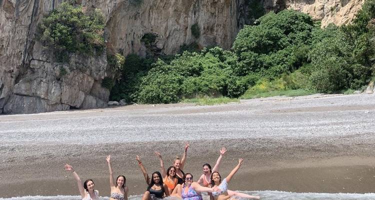 Grupo de mujeres en el agua con orilla rocosa.